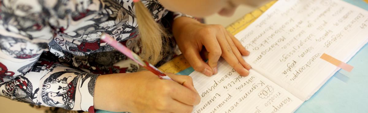 Alakouluikäinen lapsi kirjoittaa keskittyneesti vihkoon oppitunnilla.